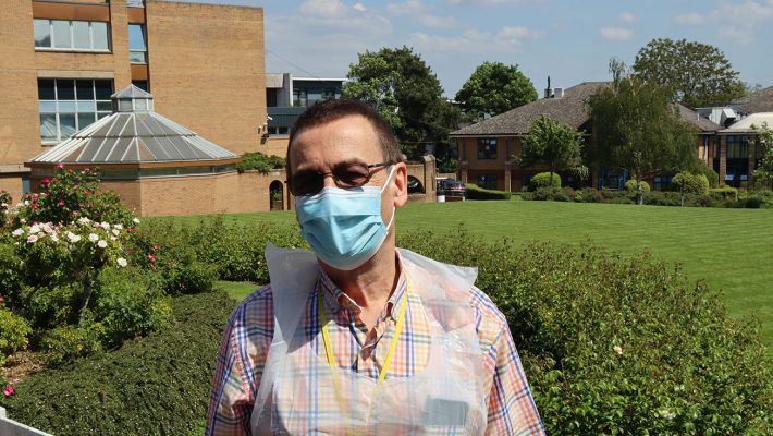 volunteer in a mask and plastic apron standing in the grounds of the RHN